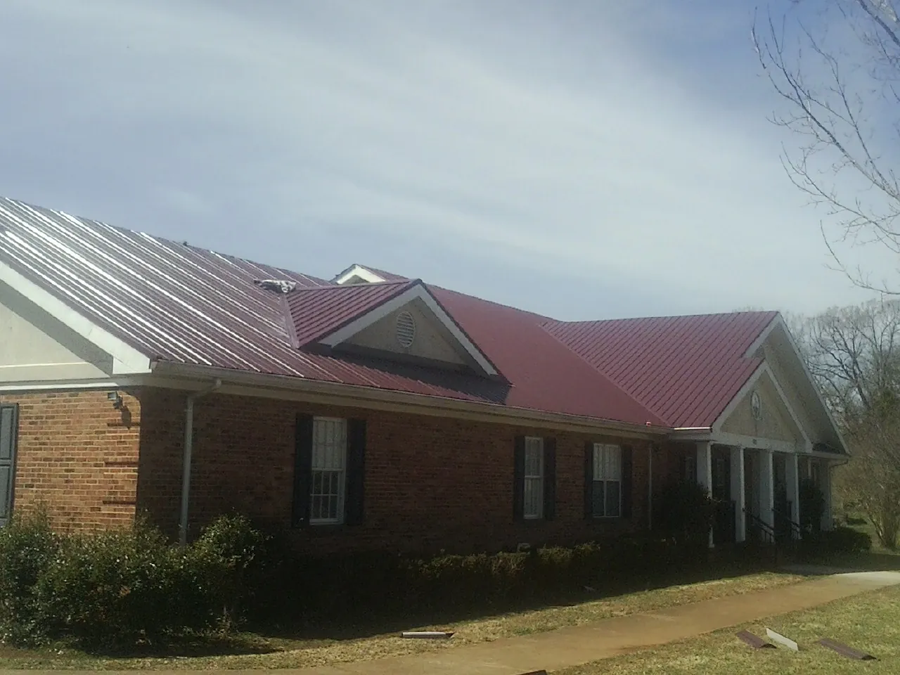 Red metal roof with gabled entries on a long brick building, from a Hail Damage Roof Repair job in Upperco