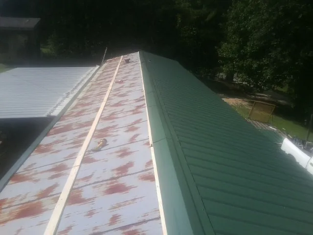 Old rusted panels beside newly installed green metal roofing — Wind Damage Roof Repair by Roofing Brothers in Upperco