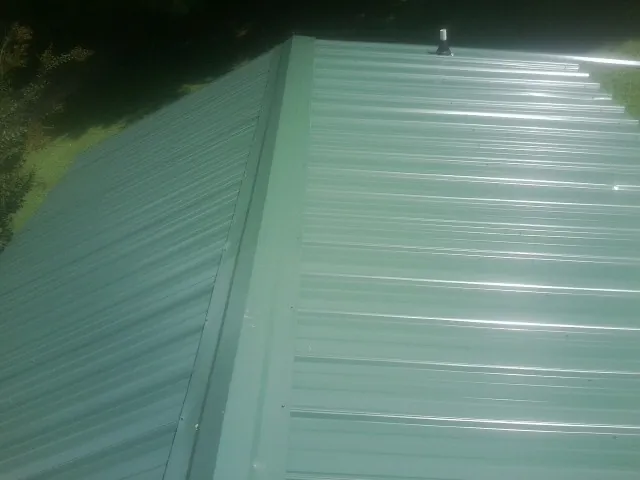 New green metal panels meeting at the ridge of a roof — Flat Roof Repair work by our crew in Upperco