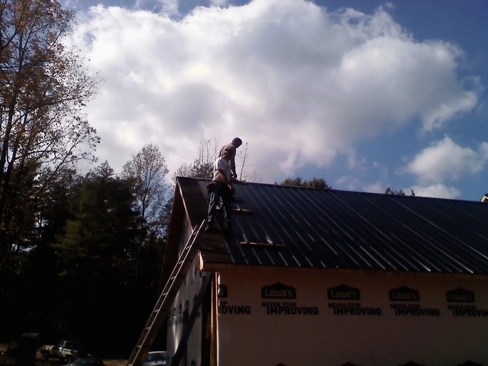 Roofer fastening dark metal panels high against a cloudy sky, from a Roof Inspection job in Upperco
