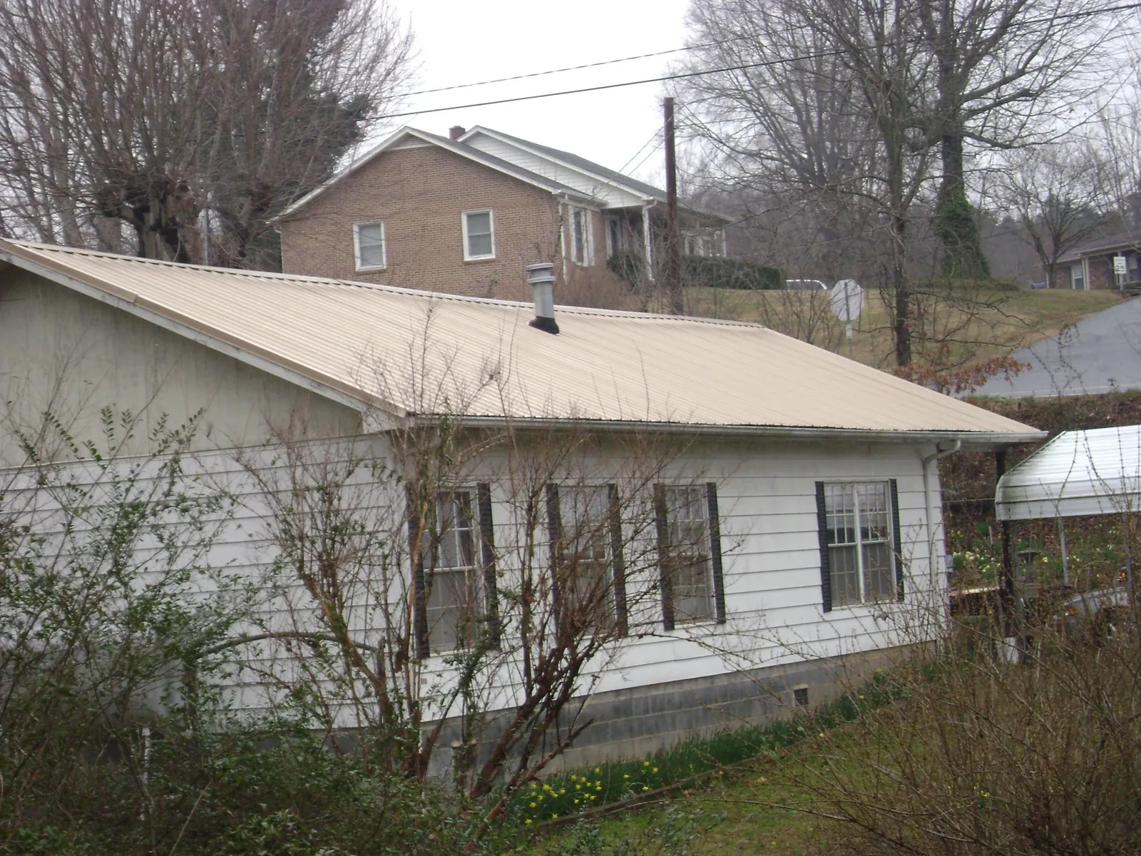 Tan metal roof on a white sided house set into a hillside — Commercial Roofing by Roofing Brothers in Upperco